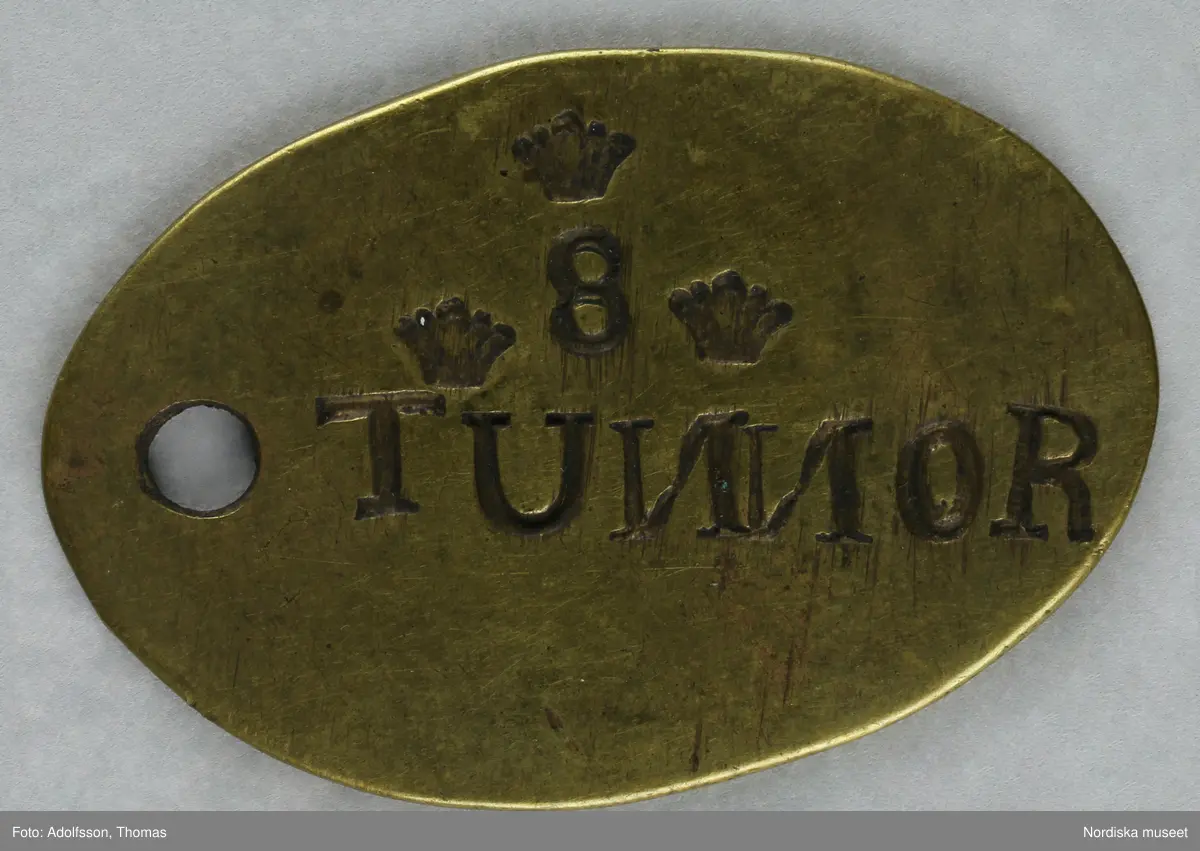 Pollett av mässing, oval. Text: 8 TUNNOR, 8:an omgiven av tre kronor.