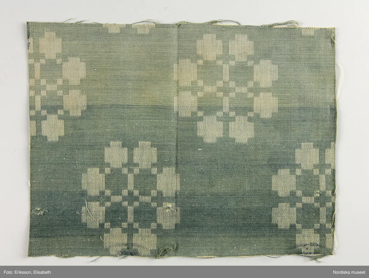 13 tygprover, varav  12 st på duktyg i förenklad damast enligt familjen Ekenmarks metod eller i rutig dräll på satin- eller kypertgrund. De flesta i rött/vitt eller blått/vitt, gult/vitt  och några helvita. I bomull, halvlinne och hellinne.
1 prov på rött möbeltyg i damast enligt Ekenmark med en upprepad snedställd blomma.
/Berit Eldvik 2012-03-06