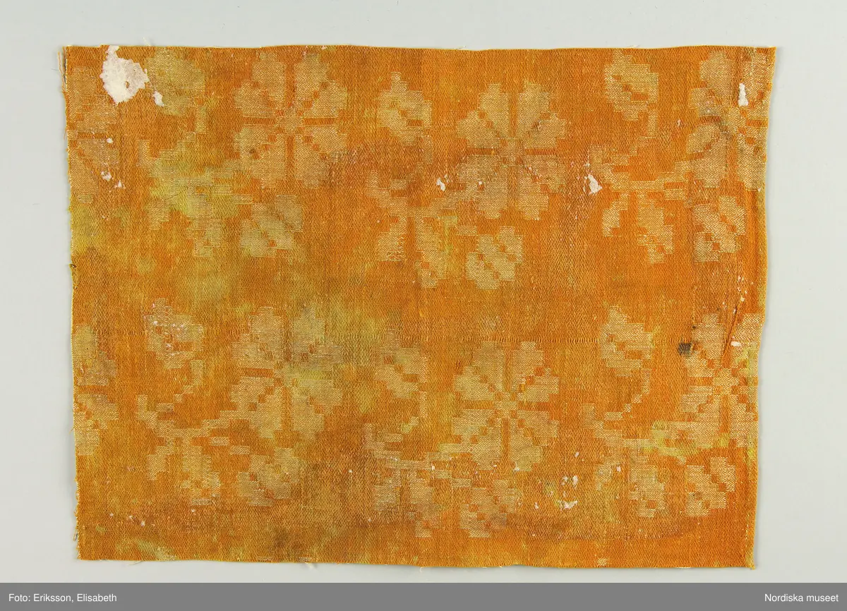 13 tygprover, varav  12 st på duktyg i förenklad damast enligt familjen Ekenmarks metod eller i rutig dräll på satin- eller kypertgrund. De flesta i rött/vitt eller blått/vitt, gult/vitt  och några helvita. I bomull, halvlinne och hellinne.
1 prov på rött möbeltyg i damast enligt Ekenmark med en upprepad snedställd blomma.
/Berit Eldvik 2012-03-06