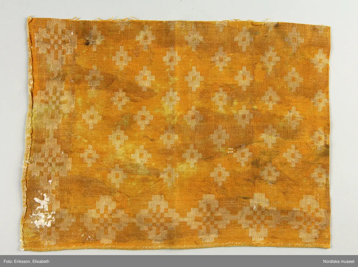 13 tygprover, varav  12 st på duktyg i förenklad damast enligt familjen Ekenmarks metod eller i rutig dräll på satin- eller kypertgrund. De flesta i rött/vitt eller blått/vitt, gult/vitt  och några helvita. I bomull, halvlinne och hellinne.
1 prov på rött möbeltyg i damast enligt Ekenmark med en upprepad snedställd blomma.
/Berit Eldvik 2012-03-06