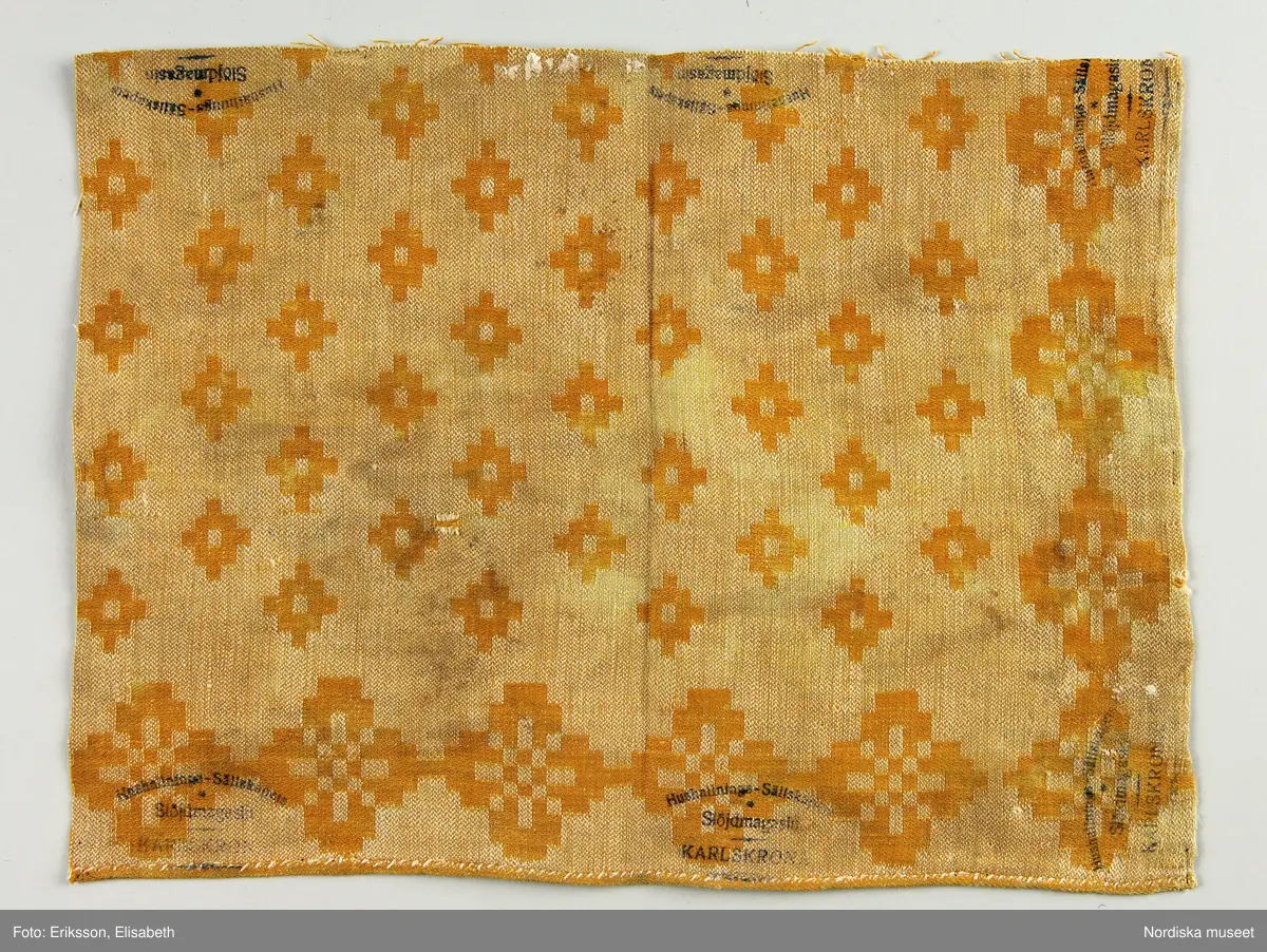 13 tygprover, varav  12 st på duktyg i förenklad damast enligt familjen Ekenmarks metod eller i rutig dräll på satin- eller kypertgrund. De flesta i rött/vitt eller blått/vitt, gult/vitt  och några helvita. I bomull, halvlinne och hellinne.
1 prov på rött möbeltyg i damast enligt Ekenmark med en upprepad snedställd blomma.
/Berit Eldvik 2012-03-06