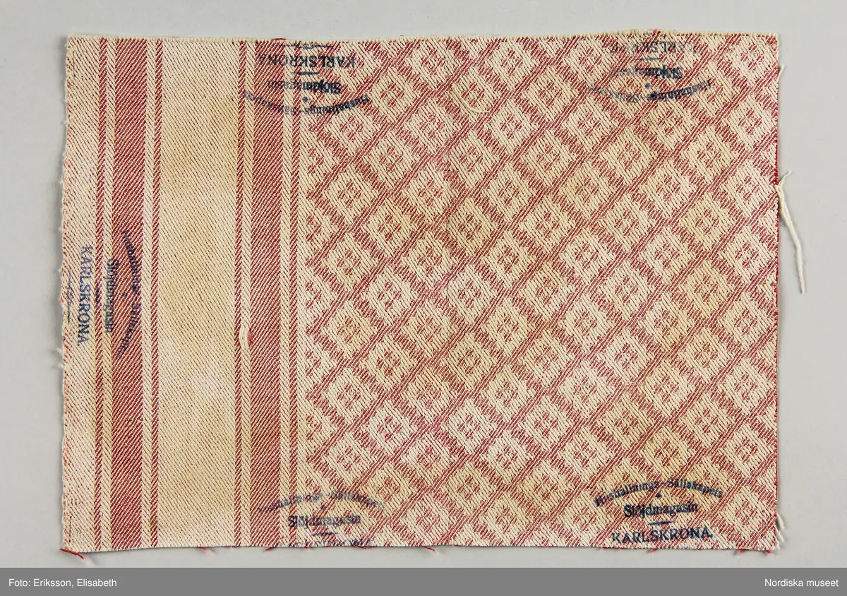 13 tygprover, varav  12 st på duktyg i förenklad damast enligt familjen Ekenmarks metod eller i rutig dräll på satin- eller kypertgrund. De flesta i rött/vitt eller blått/vitt, gult/vitt  och några helvita. I bomull, halvlinne och hellinne.
1 prov på rött möbeltyg i damast enligt Ekenmark med en upprepad snedställd blomma.
/Berit Eldvik 2012-03-06