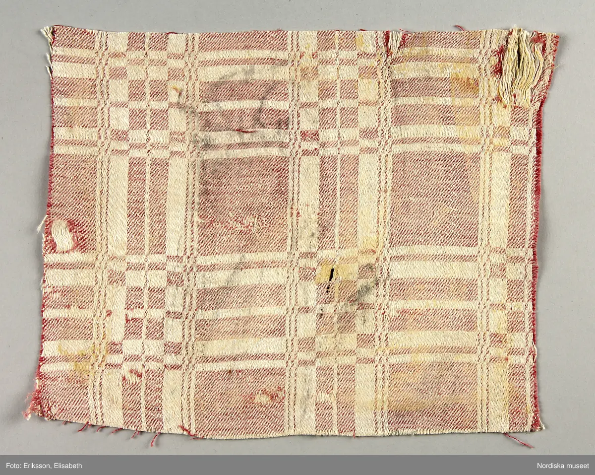 13 tygprover, varav  12 st på duktyg i förenklad damast enligt familjen Ekenmarks metod eller i rutig dräll på satin- eller kypertgrund. De flesta i rött/vitt eller blått/vitt, gult/vitt  och några helvita. I bomull, halvlinne och hellinne.
1 prov på rött möbeltyg i damast enligt Ekenmark med en upprepad snedställd blomma.
/Berit Eldvik 2012-03-06