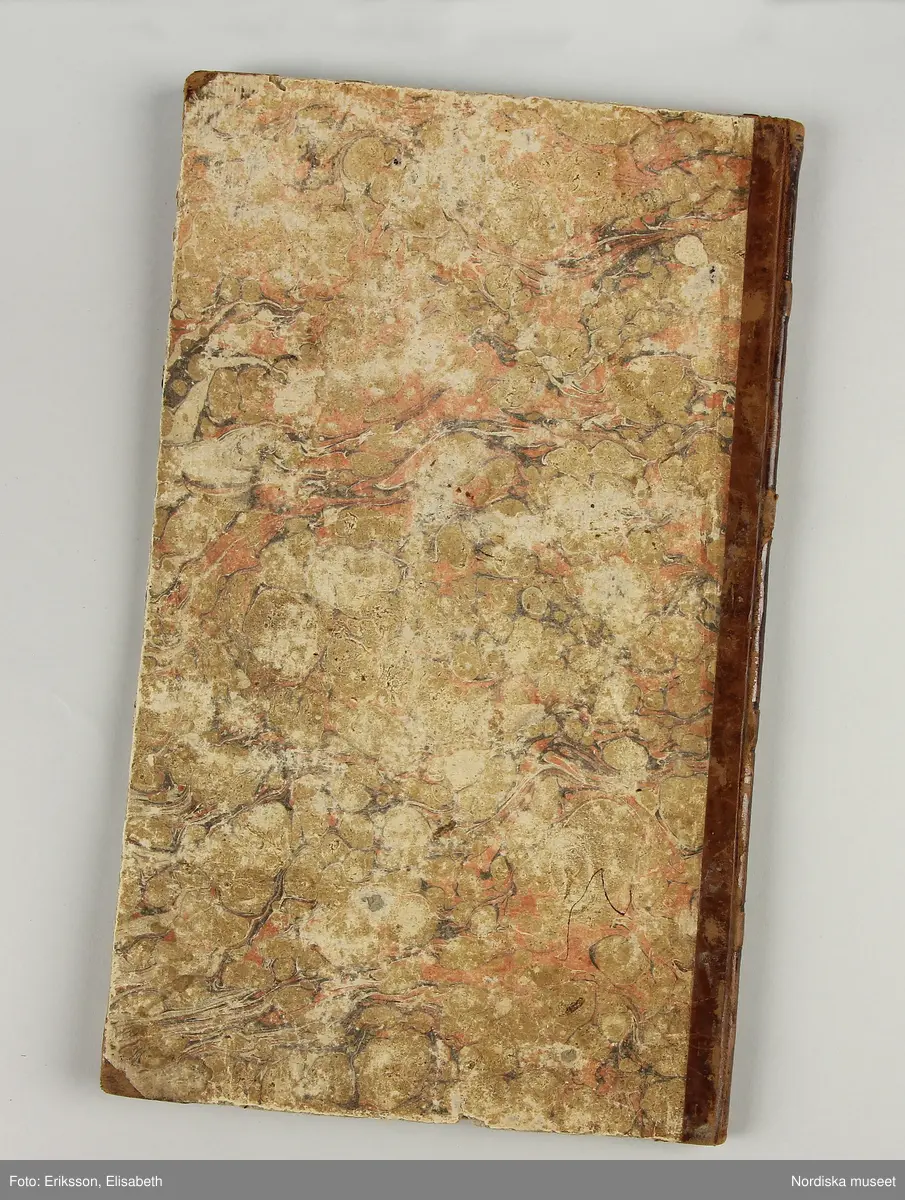 Inbunden bok med brunmarmorerade pärmar och rygg av brunt skinn. På första sidan skrivet för hand: "Wäf-Mönster-Bok för Demoisellerne Ekenmark tillhörig Anna Lithén Skara den 27 nov. 1826."
Innehåller 27 damast-och drällnotor av de vanliga slag som lärdes ut på Ekenmarks ambulerande vävkurser. Mönstrens namn påskrivna.
Bak i boken finns vävnotor och 17 tygprover på småmönstrade mångskaftade  vävnader som också lärdes ut på kurserna., samma som finns i deras tryckta läroböcker, t.ex.: nr 52 (delvis) Mönster till faconer utan veck med en bom ( hålkrus). Nr 21, stjärntyg nr 24,  blombård nr 22, wecktyg med vandringsman nr 20, 2 schalettemönster, Wästtygsmönster nr 57, Förgätmigejmönstret nr 27 samt nr. 44 2 prover.
Boken i gott skick.
Har  tillhört vävlärarinnan Johanna Brunsson, som hade känd vävskola för utbildning av vävlärare i Stockholm. Givaren  Alma Jacobbson var hennes systerdotter som tog över verksamheten efter hennes död.
/Berit Eldvik 2012-02-28