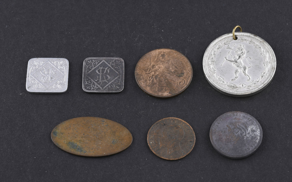 Syv mynter, medaljer og polletter i varierende størrelse og tilstand. Myntene er fra USA, Tyskland og England. Myntene og polettene var oppbevart i en liten papirpose.