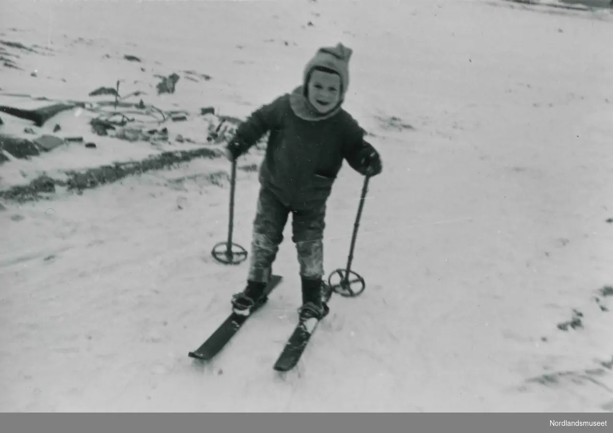 Et lite barn med strikket lue går på ski. Bildetekst: "Bakgård i Dronningens gate 3".