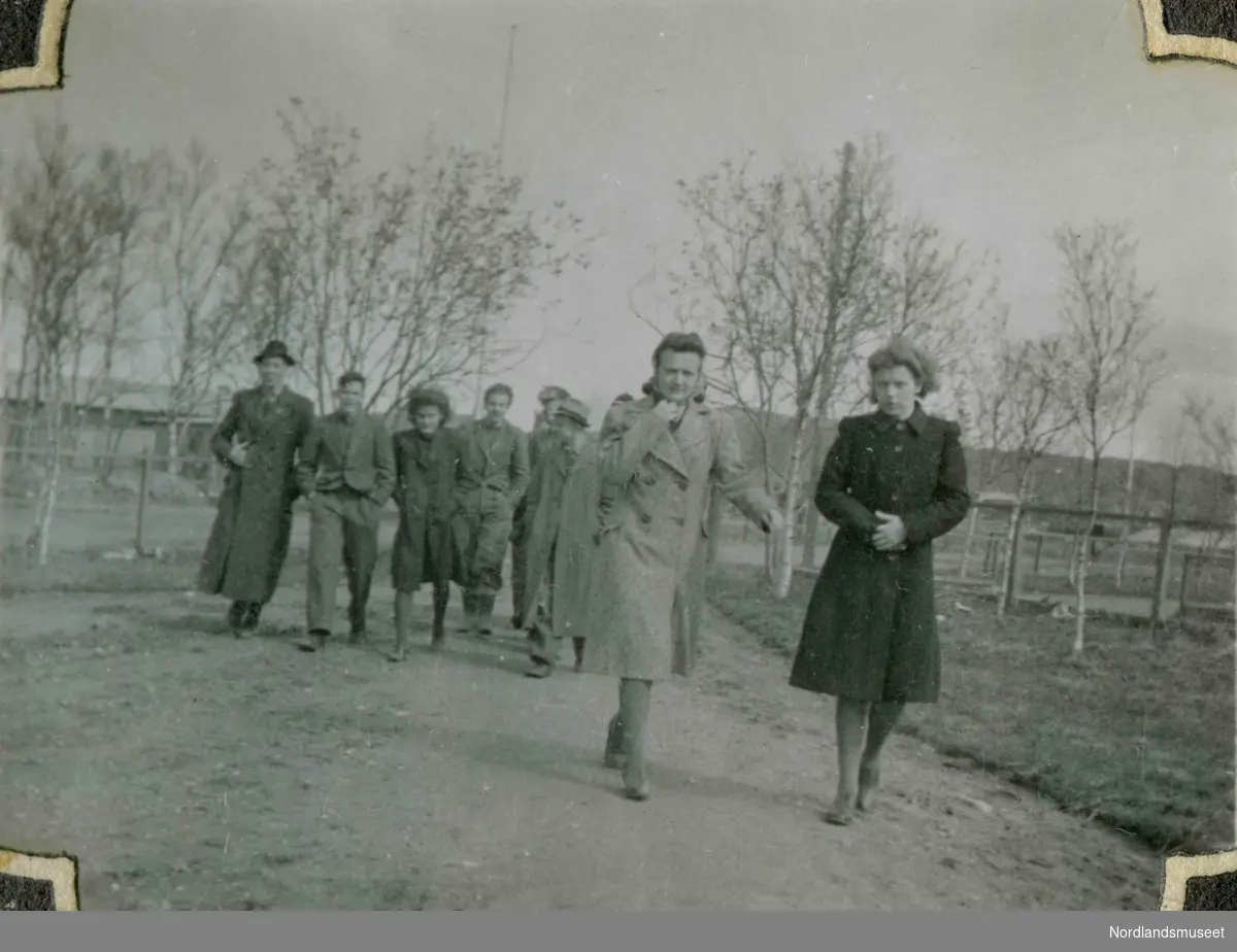 Ni unge mennesker fotografert utendørs. Alle har på seg lange frakker. Bildetekst: " På "museet" 1943".