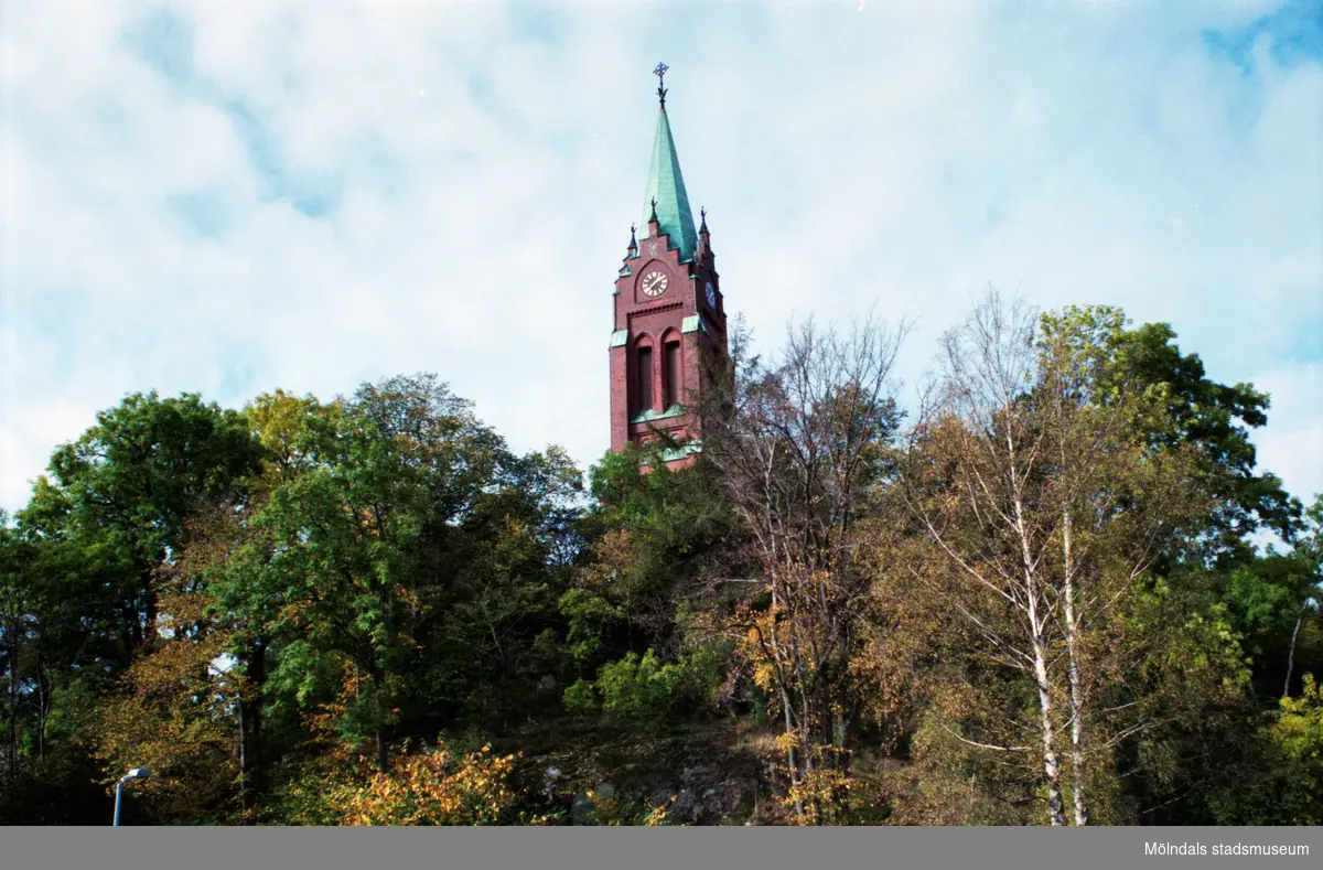 Fässbergs kyrka omgiven av grönska på berget. Mölndalsbro i dag - ett skolpedagogiskt dokumentationsprojekt på Mölndals museum under oktober 1996. 1996_0913-0930 gjorda av högstadieelever från Kvarnbyskolan 9A, grupp 1. Se även gruppbilder på klasserna 1996_1382-1405 och bilder från den färdiga utställningen 1996_1358-1381.