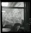 1950. Frankrike. Personer inne i ett café sedda utifrån, genom spetsgardin som hänger i skyltfönstret.