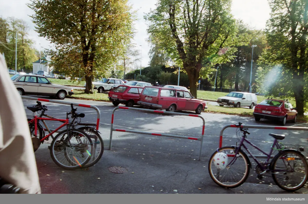 Cyklar uppställda vid en parkering. Mölndalsbro i dag - ett skolpedagogiskt dokumentationsprojekt på Mölndals museum under oktober 1996. 1996_1005-1023 är gjorda av högstadieelever från Kvarnbyskolan 9A, grupp 6. Se även 1996_0913-0940, gruppbilder på klasserna 1996_1382-1405 samt bilder från den färdiga utställningen 1996_1358-1381.