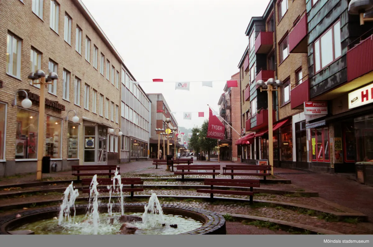 Fontän på Brogatan, västerut. Mölndalsbro i dag - ett skolpedagogiskt dokumentationsprojekt på Mölndals museum under oktober 1996. 1996_1135-1152 är gjorda av högstadieelever från Kvarnbyskolan 9D, grupp 1. Se även 1996_0913-0940, gruppbilder på klasserna 1996_1382-1405 samt bilder från den färdiga utställningen 1996_1358-1381.