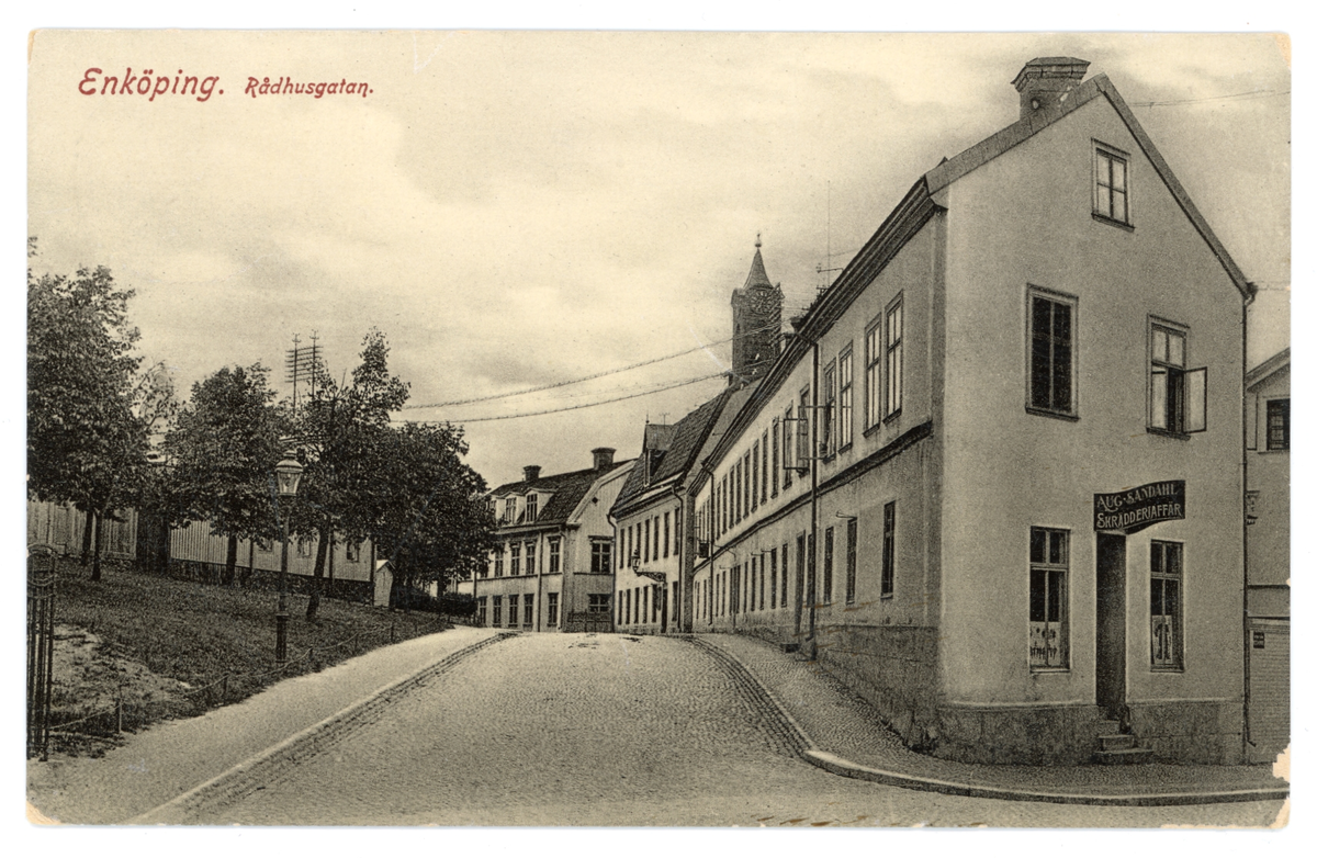 Vykort med motiv av Rådhusgatan, Enköping. Huslängan längst fram är det så kallade "strykjärnet" med skrädderiet "August Sandahl" på gaveln mot Kyrkogatan. Vykortet är poststämplat den 10/8-1917.