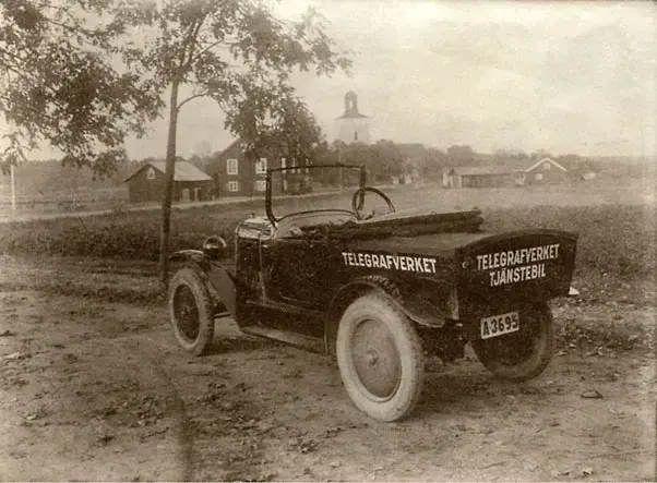 Bilen, som givetvis är huvudmotivet, är en Citroen C3 från 1925, modifierad till ”pick up” av Norrmalms karosserifabrik. Motorn var på 12 hästkrafter vilket gav en maxfart på 37 km/t. Bilen skrotas redan 1930, oklart varför men dåtidens vägar slet hårt på maskineriet och rostskyddet var dåligt. Bilen var registrerad för att färdas inom Stockholms stad vilket tydligen inte skulle ses som en begränsning för ett besök i Västerhaninge.
Målet för besöket var telefonstationen, inrymd i konsumaffären, bakom ryggen på fotografen. Fastigheten kallades Ryborg och innehöll även bostäder för bl.a. konsum- och telegrafanställda. Ryborg låg som första hus på höger sida av vägen upp mot Ribbygårdarna (nuvarande Blåkullavägen 2–4).
I bakgrunden ser vi Tingshuset med uthus. Tingsrätten hade tio år tidigare flyttat in till Stockholm. Här fanns vid denna tidpunkt ett par små lägenheter och de stora salarna användes vid olika typer av sammankomster. Till höger om kyrkan syns Kaplansgården med ett par lägenheter. Här bodde bland annat barnmorskan.
Av husen på bilden och det ej synliga Ryborg är endast Västerhaninge kyrka och Tingshuset, nu hembygdsgård, kvar idag. 
