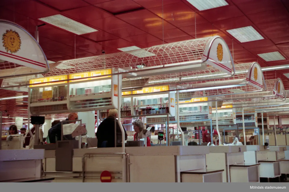 Kassorna i en livsmedelsbutik (Hemköp) på Brogatan. Mölndalsbro i dag - ett skolpedagogiskt dokumentationsprojekt på Mölndals museum under oktober 1996. 1996_1264-1282 är gjorda av högstadieelever från Åbyskolan 8A, grupp 2. Se även 1996_0913-0940, gruppbilder på klasserna 1996_1382-1405 och bilder från den färdiga utställningen 1996_1358-1381.