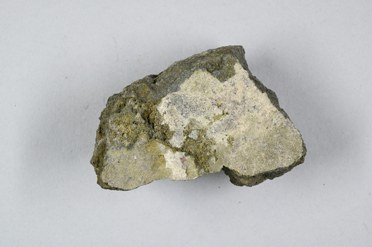 Mineralprov, grå, grön-vitaktig. Tillhörande lapp med notering: "23. Gruner Ofengalmei (?)".