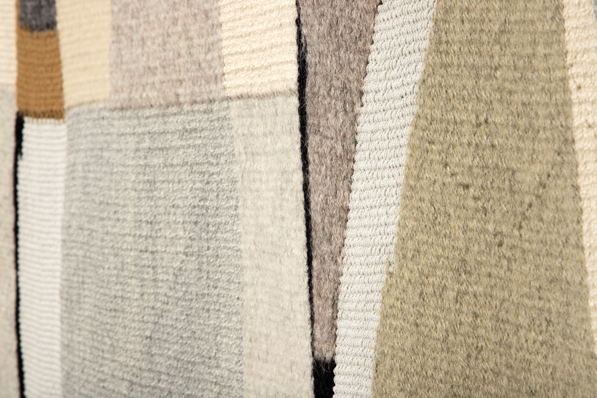 I grå, beige, gule og sorte toner vises et motiv av firkantede og trekantede fargefelt. Mellom de skrå linjene fremhever vevteknikken skillene mellom fargefeltene.