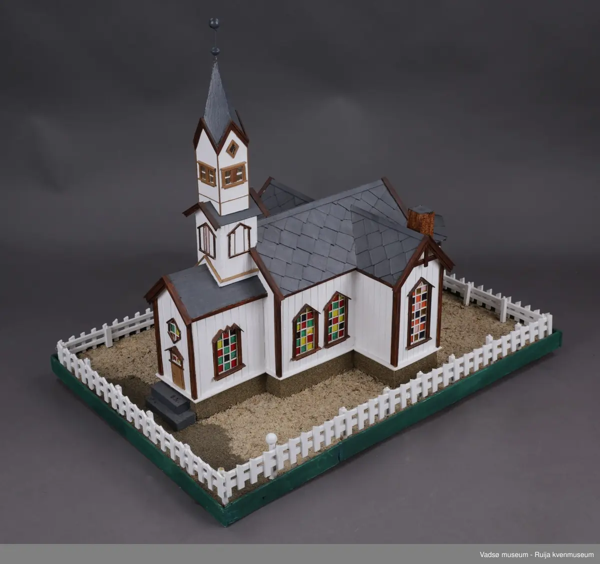 Vadsø kirke  og stakittgjerdet som omgir kirka. Vadsø kirke ble vigslet 3. oktober 1861. En stilig og rikt utsmykket kirke, som hele byens befolkning var glad i, og der alle store høytider ble markert...Altertavla var en kopi av Adolf Tiedemanns maleri i Trefoldighetskirken i Oslo. Under tyskernes tilbaketog, natten mellom 28. og 29. oktober 1944, brant kirka ned til grunnen.