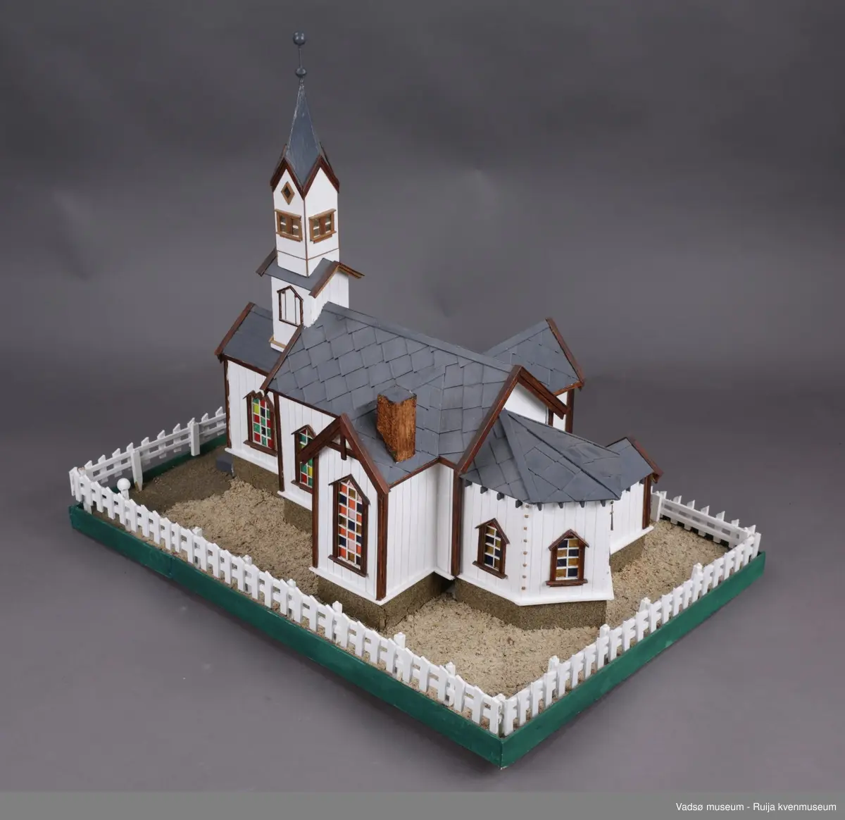 Vadsø kirke  og stakittgjerdet som omgir kirka. Vadsø kirke ble vigslet 3. oktober 1861. En stilig og rikt utsmykket kirke, som hele byens befolkning var glad i, og der alle store høytider ble markert...Altertavla var en kopi av Adolf Tiedemanns maleri i Trefoldighetskirken i Oslo. Under tyskernes tilbaketog, natten mellom 28. og 29. oktober 1944, brant kirka ned til grunnen.