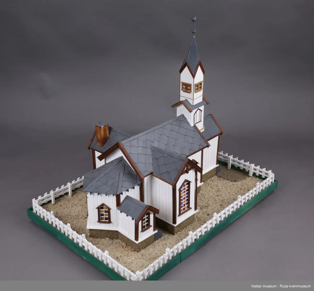Vadsø kirke  og stakittgjerdet som omgir kirka. Vadsø kirke ble vigslet 3. oktober 1861. En stilig og rikt utsmykket kirke, som hele byens befolkning var glad i, og der alle store høytider ble markert...Altertavla var en kopi av Adolf Tiedemanns maleri i Trefoldighetskirken i Oslo. Under tyskernes tilbaketog, natten mellom 28. og 29. oktober 1944, brant kirka ned til grunnen.