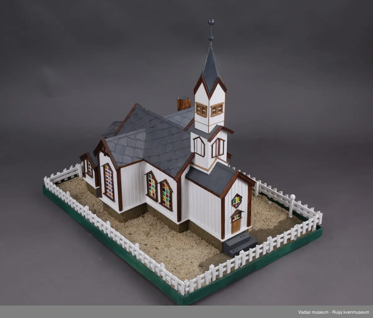 Vadsø kirke  og stakittgjerdet som omgir kirka. Vadsø kirke ble vigslet 3. oktober 1861. En stilig og rikt utsmykket kirke, som hele byens befolkning var glad i, og der alle store høytider ble markert...Altertavla var en kopi av Adolf Tiedemanns maleri i Trefoldighetskirken i Oslo. Under tyskernes tilbaketog, natten mellom 28. og 29. oktober 1944, brant kirka ned til grunnen.
