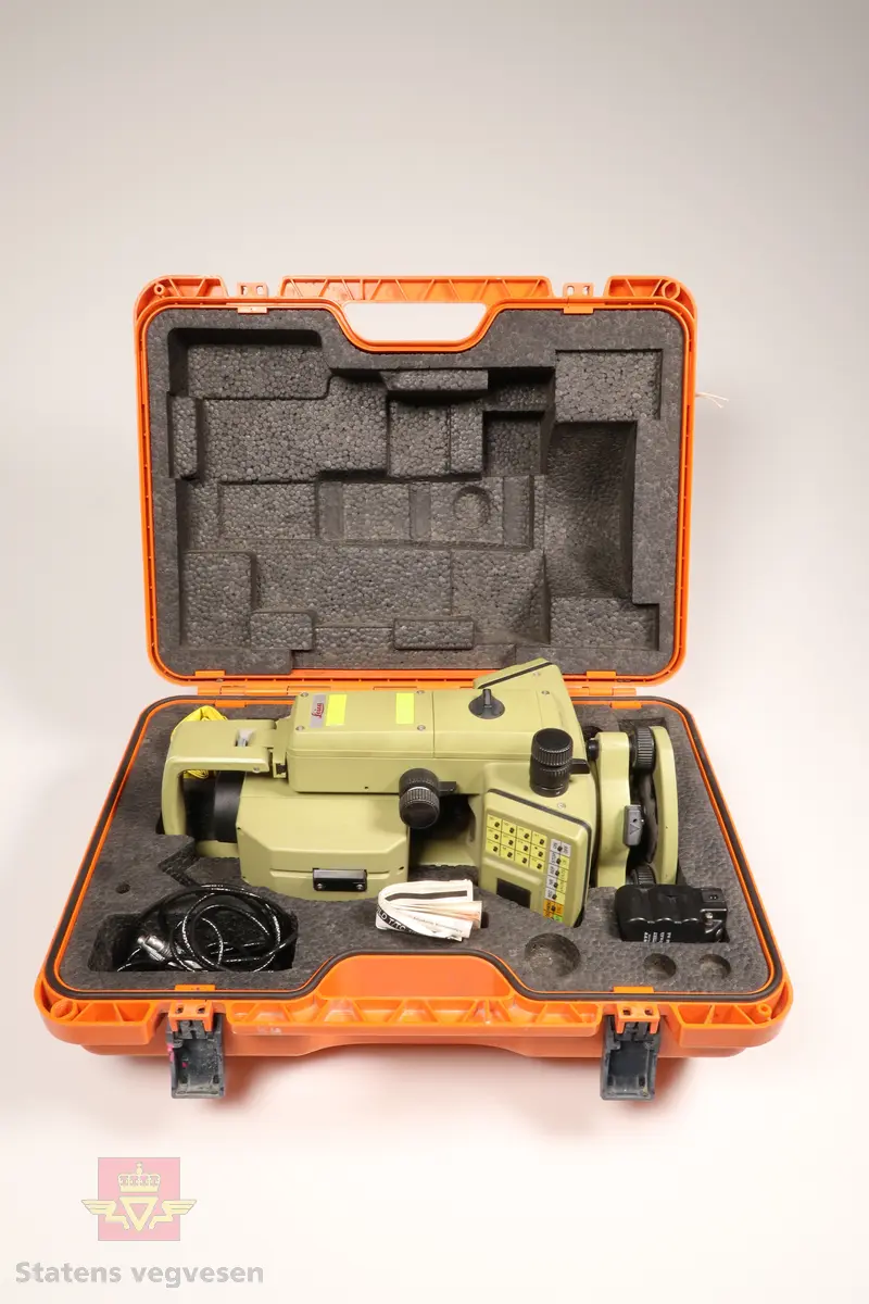 Grønn og svart totalstasjon med oransje koffert. I kofferten er det en totalstasjon oppå en GDF22 Fotplate, regntrekk, instruksjonsmanual og en LEMO ledning.