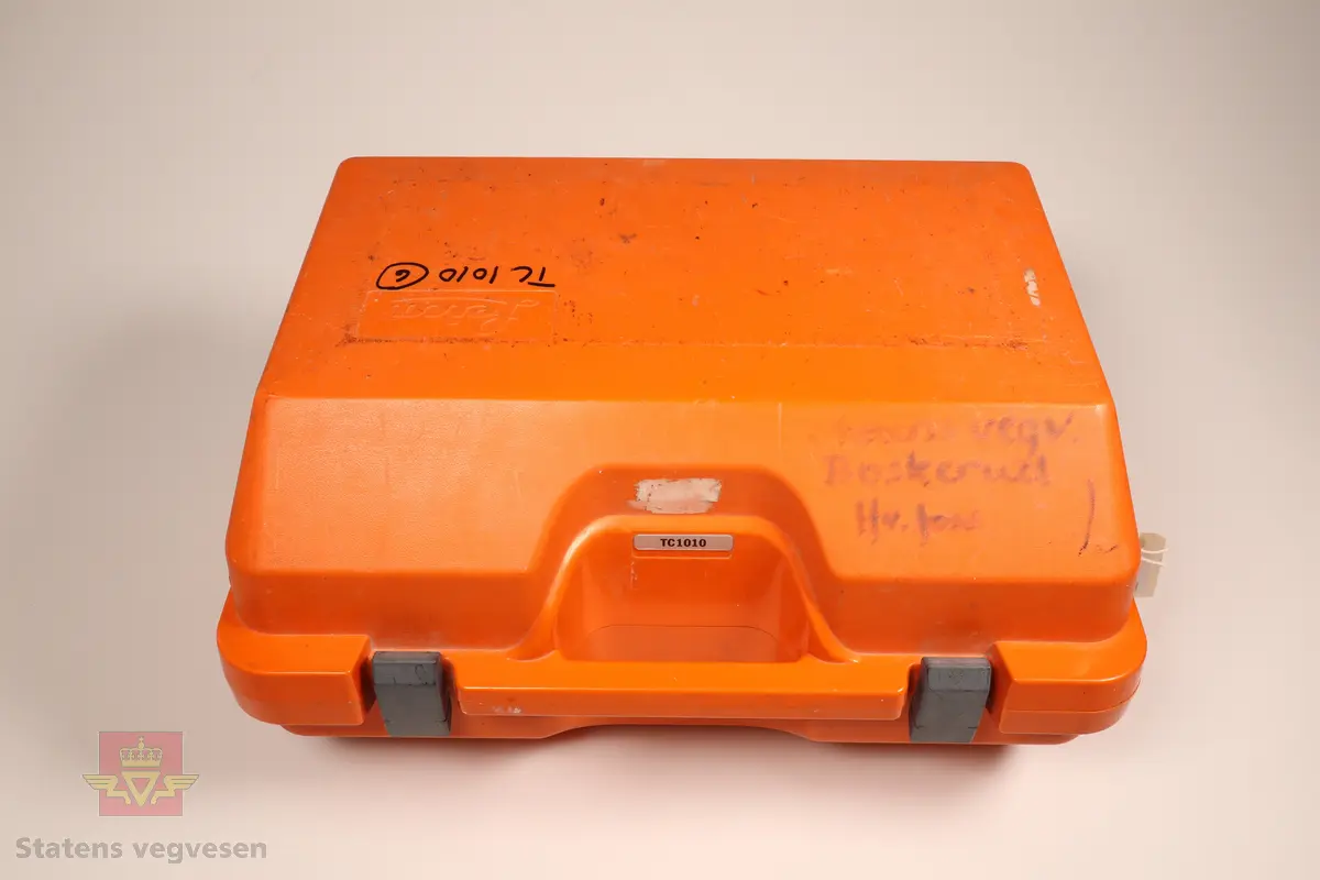 Grønn og svart totalstasjon med oransje koffert. I kofferten er det en totalstasjon oppå en GDF22 Fotplate, regntrekk, instruksjonsmanual og en LEMO ledning.