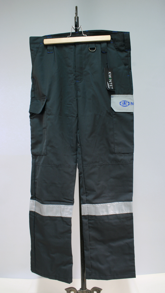 Sort uniform bestående av kortermet poloskjorte, bukser og skyggelue med Nokas-logo, og tilhørende belte rigget med lommelykt og walkie-talkie.
