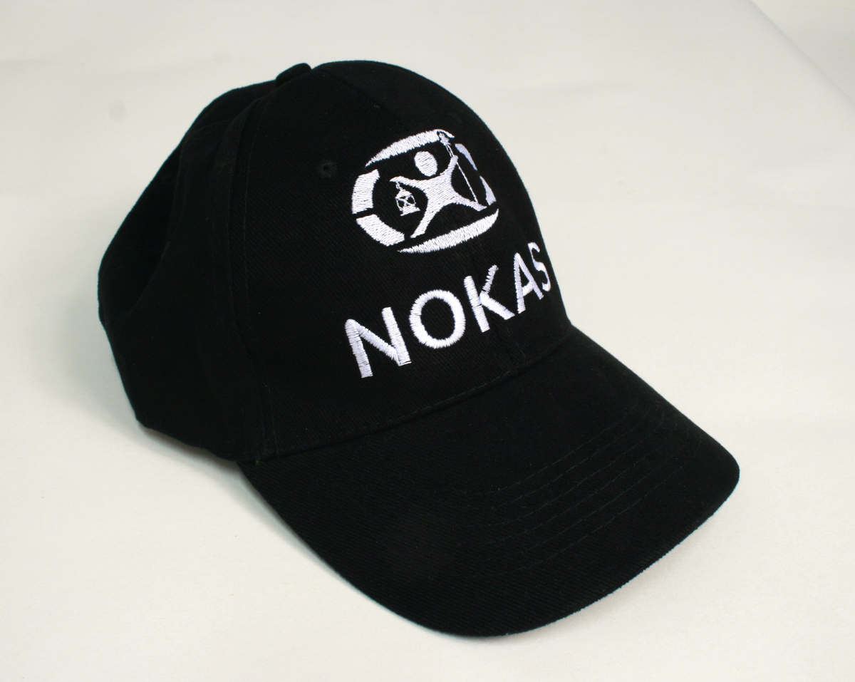 Sort uniform bestående av kortermet poloskjorte, bukser og skyggelue med Nokas-logo, og tilhørende belte rigget med lommelykt og walkie-talkie.