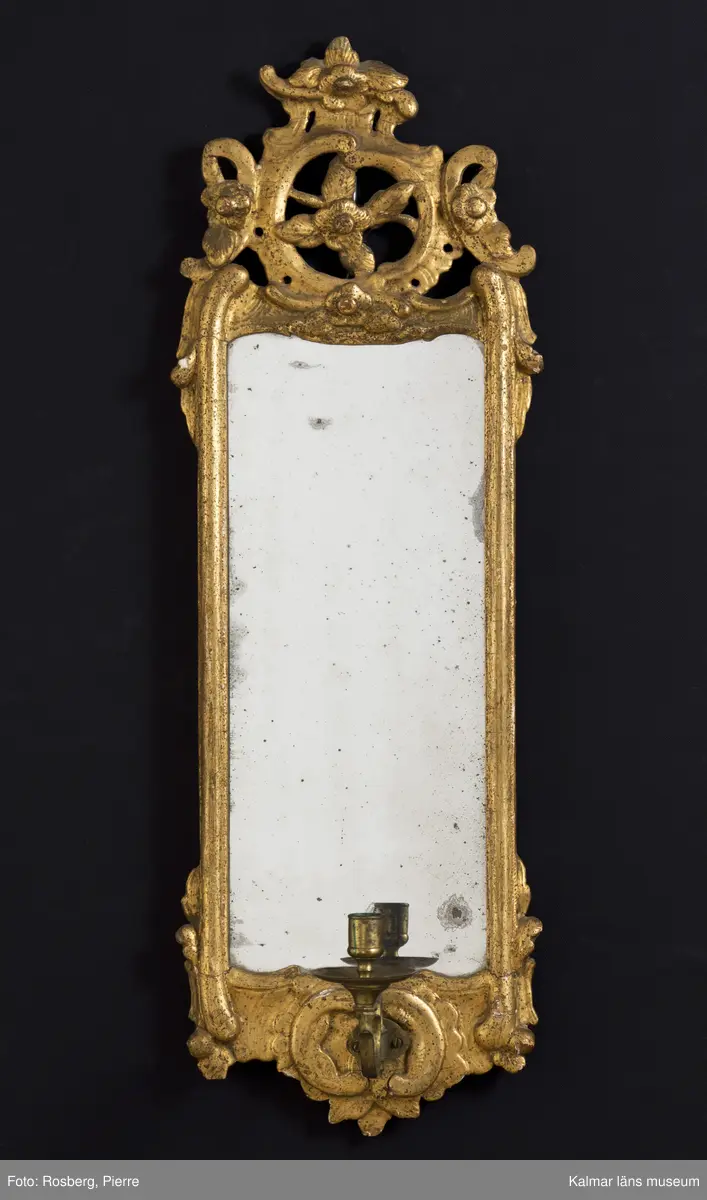 KLM 24949:1-2. Spegellampett, ett par. Guldbronserade ramar av trä med spår efter ursprunglig förgyllning. Rocaille-ornament med tjock kredering överst. Några små olikheter i de båda speglarnas dekor. Otydlig signatur på baksidan. Löstagbara ljuhållare av mässing.