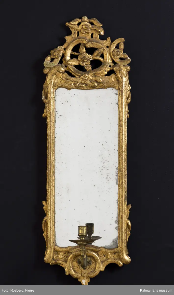 KLM 24949:1-2. Spegellampett, ett par. Guldbronserade ramar av trä med spår efter ursprunglig förgyllning. Rocaille-ornament med tjock kredering överst. Några små olikheter i de båda speglarnas dekor. Otydlig signatur på baksidan. Löstagbara ljuhållare av mässing.