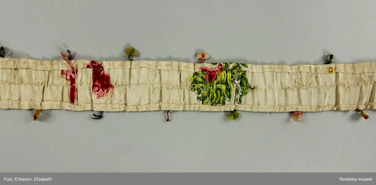 Brudklänning (robe), av broscherat, vitbottnat kinesiskt siden. Nygjord framvåd av fint vitt bomullstyg med kjolvolang nedtill av robens tyg. Två lösa garneringsbårder.