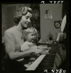 Sångerskan Alice Babs spelar på ett piano med ett barn i knä