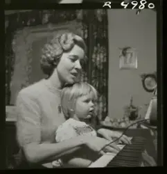 Sångerskan Alice Babs spelar på ett piano med ett barn i knä