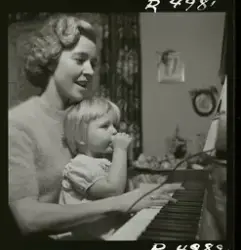 Sångerskan Alice Babs spelar på ett piano med ett barn i knä