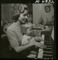 Sångerskan Alice Babs spelar på ett piano med ett barn i knä