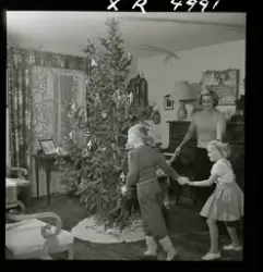 Sångerskan Alice Babs och tre barn dansar kring en julgran.