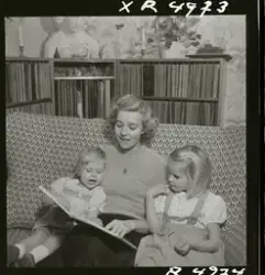 Sångerskan Alice Babs sitter i en soffa och läser saga för t