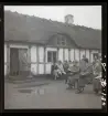 En man ståendes på trappstegen in till ett hus håller ett tal. Publik sitter framför. Skansen, Stockholm.