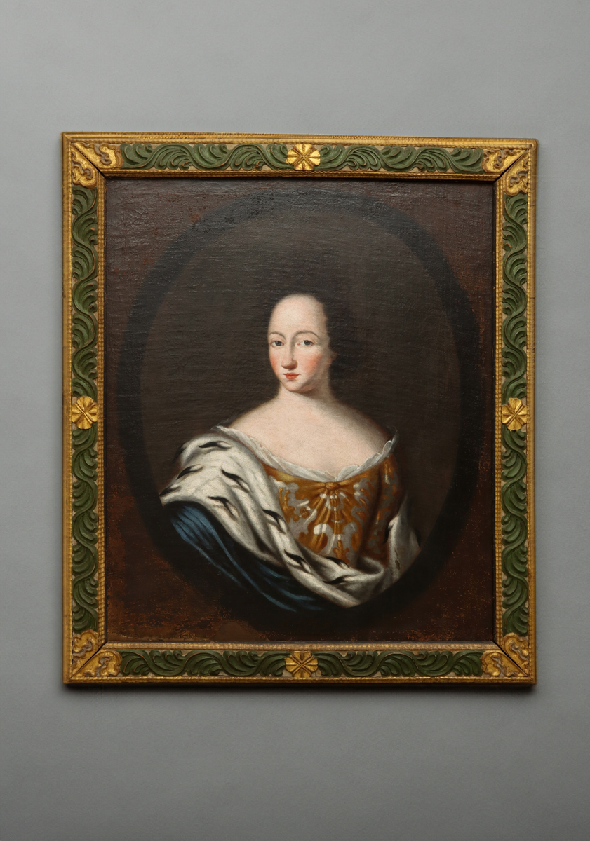 Bröstbild av Ulrika Eleonora den äldre, i fas åt vänster, i en svart oval mot brun botten. Klädd i en dräkt med djup båtringad urringning av guldbrokad med vit spets och en mantel av blått tyg kantad med päls av hermelin. Med en lös, lockig och mörk frisyr med hög panna och med accentuerade ögonbryn, kinder och läppar.