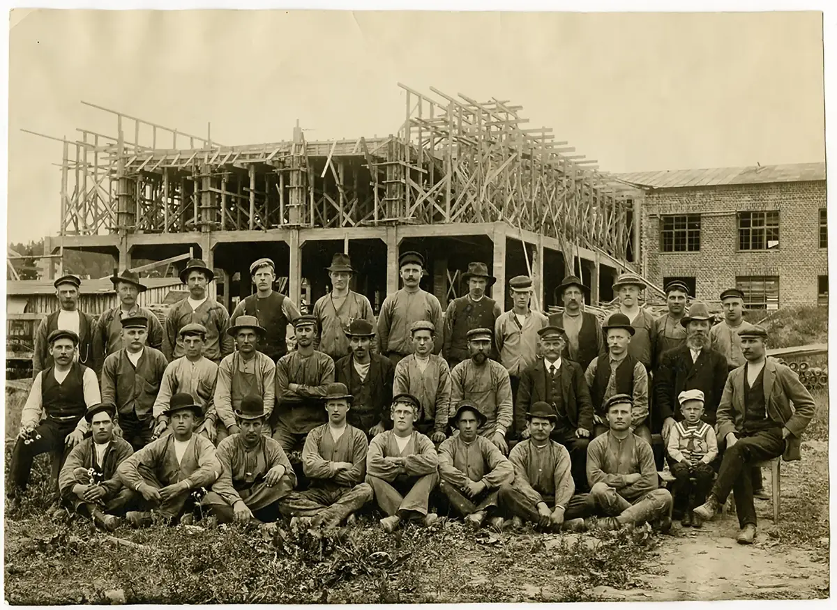 Optimus fabrik för tillverkning av fotogenlampor, brännare och kök stod klar 1908.
Optimusfabriken var en av de första byggnaderna i landet som uppfördes med stomme i betong.
Här är byggstyrkan samlad 1907.