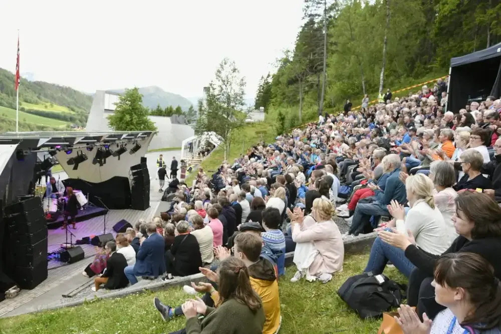 Festivalområde med publikum som sit i amfi og på graset og klappar for artist på scena