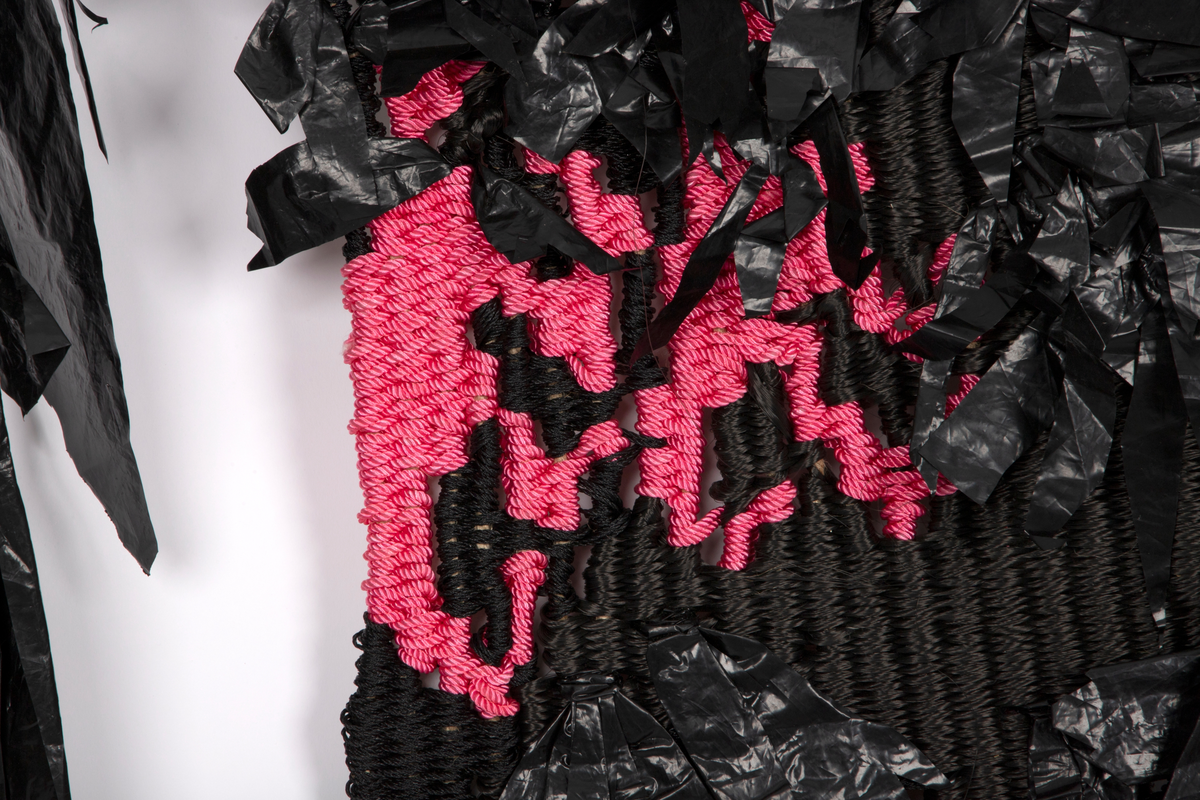 Svart ørn med rosa nebb og klør, vevd i nylon og polyester. Vinger, stjerten og fjærpryd på magen er laget av svart plast.