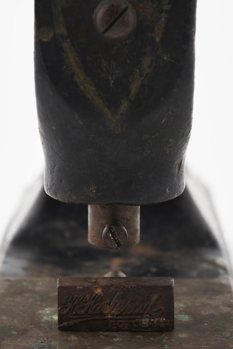 Signaturstempel i jern. Håndtaket presses ned og merker papir eller fotografi med fotografens stempel. Følgende logo presses inn:  H. Haslerud. FOTOGRAF

Diverse fotoutstyr og andre gjenstander som har tilhørt Synnøve Brændshøi sitt fotoatelier. De fleste er nok fra 40- og 50-tallet. 