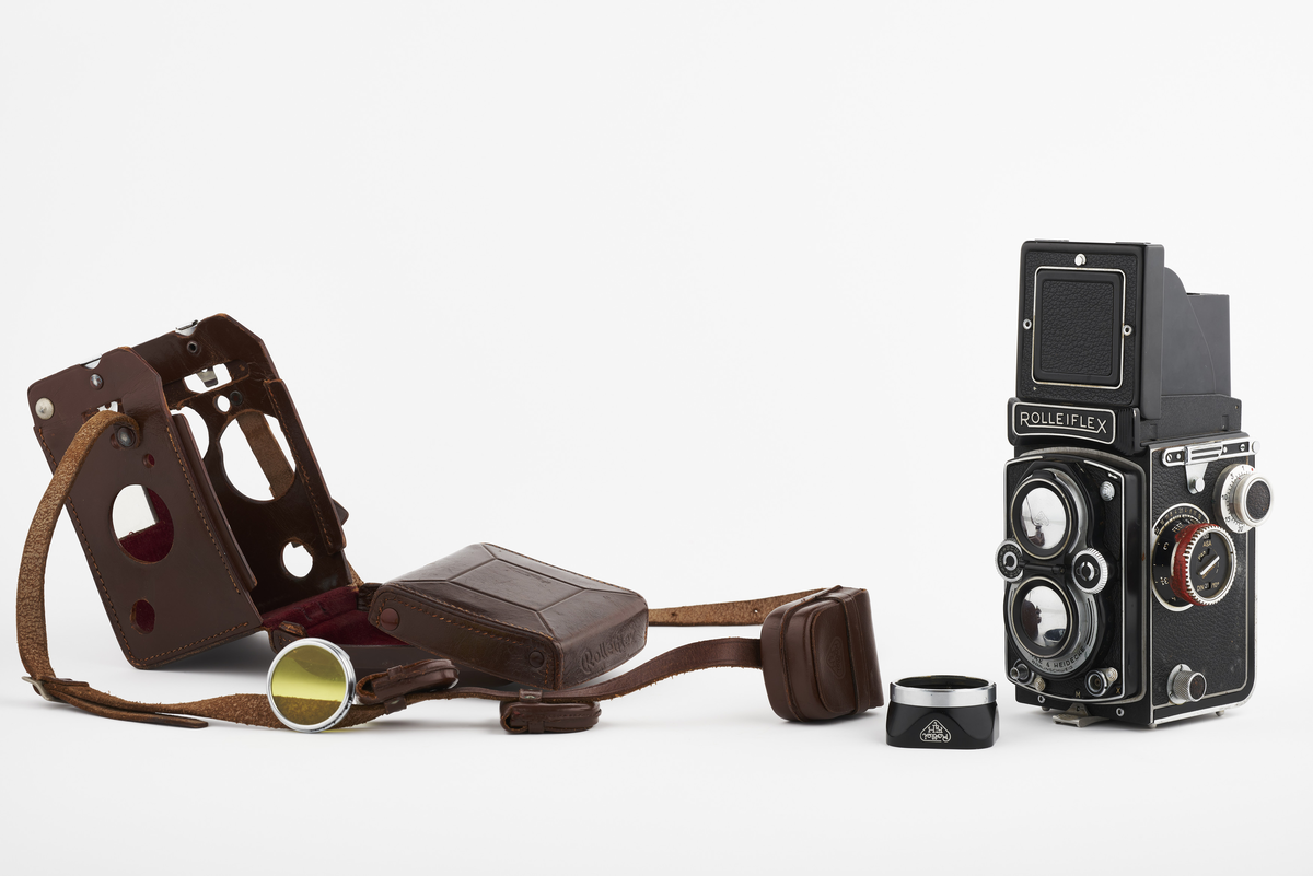 Kamera med tilhørende futteral/veske i brunt lær med fløyel på innsiden. Kameraet er et twin lens av merke Rolleiflex, trolig av modellen 2.8, produsert fra 1949 til 1956. Det har en Heidosmat 1:2,8/75 linse. Kameraetuiet har små vesker med diverse tilbehør. Har tilhørende bruksanvisning på tysk, med manglende forside.

Samlingen består av diverse fotoutstyr og andre gjenstander som har tilhørt Synnøve Brændshøi sitt fotoatelier. De fleste er nok fra 1940- og 50-tallet.