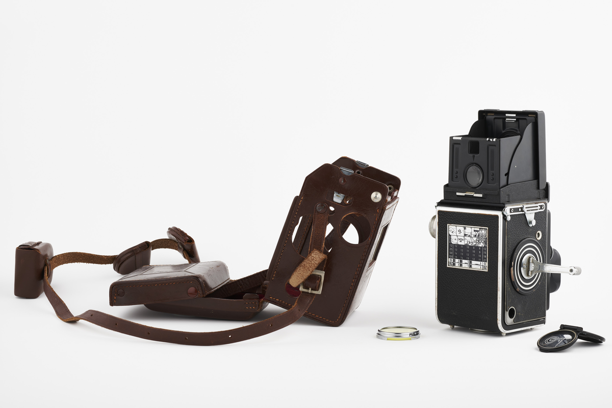 Kamera med tilhørende futteral/veske i brunt lær med fløyel på innsiden. Kameraet er et twin lens av merke Rolleiflex, trolig av modellen 2.8, produsert fra 1949 til 1956. Det har en Heidosmat 1:2,8/75 linse. Kameraetuiet har små vesker med diverse tilbehør. Har tilhørende bruksanvisning på tysk, med manglende forside.

Samlingen består av diverse fotoutstyr og andre gjenstander som har tilhørt Synnøve Brændshøi sitt fotoatelier. De fleste er nok fra 1940- og 50-tallet.