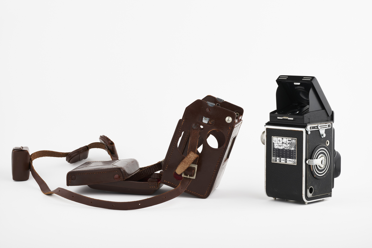 Kamera med tilhørende futteral/veske i brunt lær med fløyel på innsiden. Kameraet er et twin lens av merke Rolleiflex, trolig av modellen 2.8, produsert fra 1949 til 1956. Det har en Heidosmat 1:2,8/75 linse. Kameraetuiet har små vesker med diverse tilbehør. Har tilhørende bruksanvisning på tysk, med manglende forside.

Samlingen består av diverse fotoutstyr og andre gjenstander som har tilhørt Synnøve Brændshøi sitt fotoatelier. De fleste er nok fra 1940- og 50-tallet.