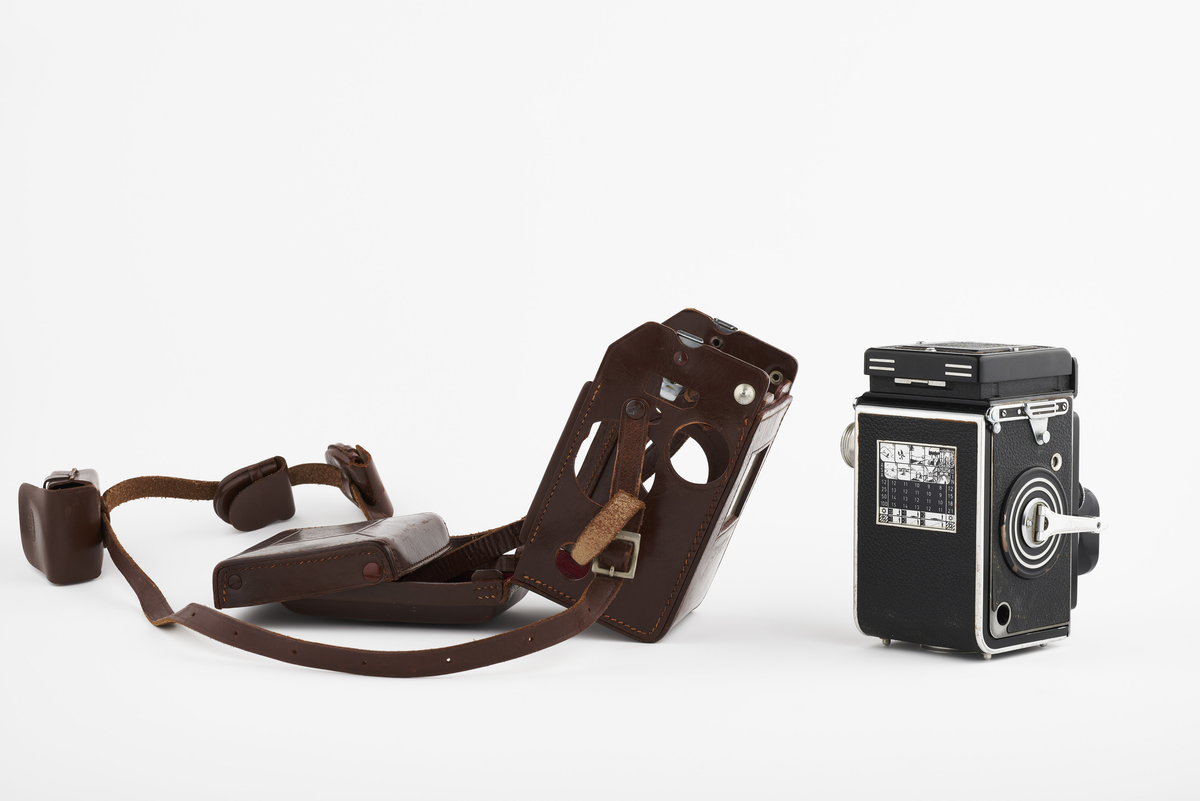 Kamera med tilhørende futteral/veske i brunt lær med fløyel på innsiden. Kameraet er et twin lens av merke Rolleiflex, trolig av modellen 2.8, produsert fra 1949 til 1956. Det har en Heidosmat 1:2,8/75 linse. Kameraetuiet har små vesker med diverse tilbehør. Har tilhørende bruksanvisning på tysk, med manglende forside.

Samlingen består av diverse fotoutstyr og andre gjenstander som har tilhørt Synnøve Brændshøi sitt fotoatelier. De fleste er nok fra 1940- og 50-tallet.