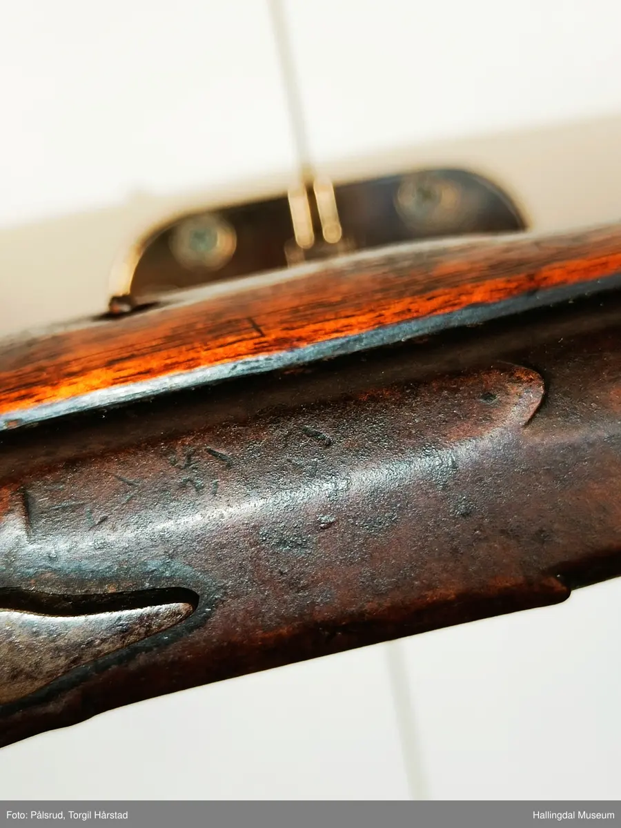 Gevær med perkusjonslås og kassepipe. Har mest sannsynlig vært ombygd fra flintlås. Geværet har kassepipe - har firkantet løp bakerst fra låsen til siktet midt på løpet. Fra låsen til siktet midt på løpet er løpet kasseformet og har en dekorert overgang til et svakt avrundet åttekantet løp. Det fremste siktet er av messing. Kolbekappen er festet med to skruer. Mangler avtrekksbøyle, reim og ladestokk. Montert på patentsvansskrue ved ombygging. Løpet er 15 cm i diameter og glattløpet.
