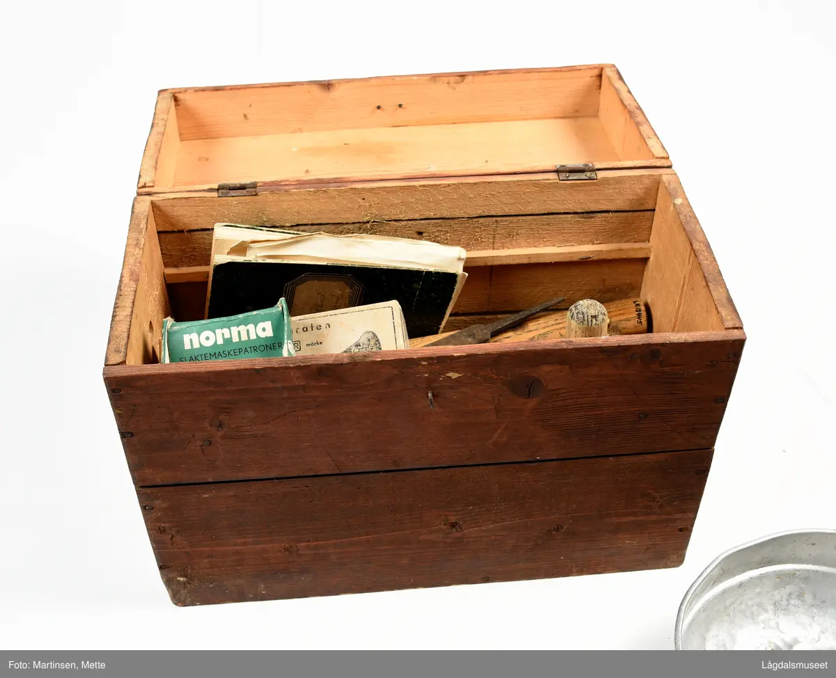 Kiste eller utstyrkiste til diverse redskaper for slakting. Kista er av tre og trolig lagd av materialer fra en margarinkasse. Jamnfør stempel på bunnen. Hengslet lokk med håndtak. Krok foran til låsing. Malt i en rødbrun farge.