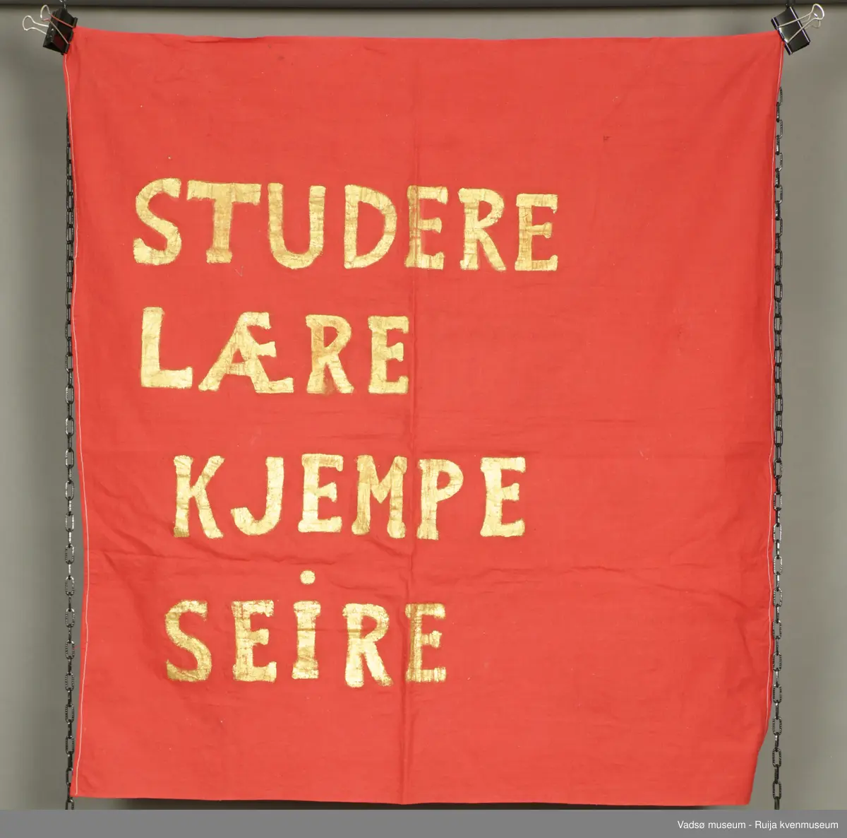 Rødt banner med slagordet "Studere, lære, kjempe, seire".